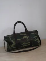 Bolso de lona color negro con detalles en cuero color tostado. Tiene doble asa de mano y correa de hombro ajustable y extraíble.