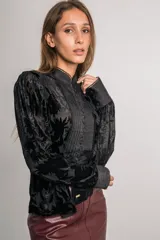 Camisa negra de terciopelo con motivos florales, cuello mao, mangas abullonadas, detalles plisados en el frente, botones forrados y bordes con puntilla.
