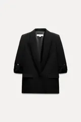 Blazer negro abierta de cuello solapa y hombreras. Manga por debajo del codo acabada en vuelta con trabilla y botón dorado. Bolsillos delanteros con solapa.