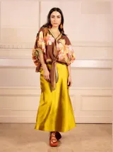 Camisa marrón estampada con hibiscos y líneas, con detalle de hilos dorados, botones y lazo para anudar.