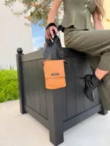 Bandolera tipo phone bag pequeña, color marrón claro, con correa de galón regulable. Tiene un compartimento principal y un bolsillo adicional con tapa.