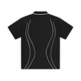Camiseta polo negra de manga corta con cuello blanco y ribetes blancos en los hombros. Presenta un pequeño logo bordado en el pecho y líneas curvas blancas a los costados del torso.