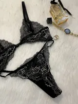 Conjunto de lencería de encaje negro con blanco, compuesto por un corpiño triangular con breteles regulables y cierre de gancho delantero, y una tanga regulable.