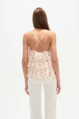Top sin mangas de poliéster, color crema con estampado floral en tonos rosados. Presenta escote en V con volados en cascada y tirantes finos.