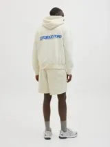 Buzo con capucha color crema, de manga larga y corte holgado. Tiene bolsillo tipo canguro y logo estampado en el pecho.