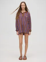 Chomba de algodón a rayas verticales color marrón, lila y blanco, de corte oversize con cuello camisero y puños en color marrón.