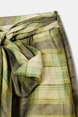 Falda corta de tiro medio con estampado de cuadros en tonos verdes y beige. Presenta un detalle de cinturón tipo lazada confeccionado en el mismo tejido y cierre lateral con cremallera oculta en costura.