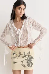 Top blanco de encaje con escote en V, volados y mangas largas con lazos.