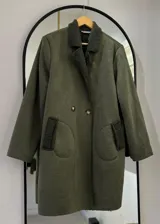 Tapado largo color verde militar, con exterior de gamuza e interior de corderito. Tiene cuello clásico, cierre frontal con doble botonadura y bolsillos de parche redondeados.