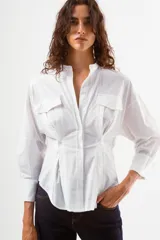 Camisa de manga larga color azul con finas rayas verticales blancas. Presenta cuello mao, botones frontales y dos bolsillos de parche con tapa en el pecho. La prenda tiene un diseño ajustado en la cintura con pinzas y un volumen holgado en las mangas.