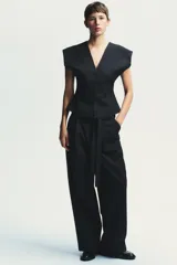 Pantalón negro con finas rayas verticales blancas, de tiro alto y corte ancho. Incluye cinturón de lazo en el mismo tejido, bolsillos laterales y pinzas.