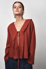 Blusa color ladrillo confeccionada en lino 100%. Tiene cuello fluido, mangas largas acampanadas y espalda descubierta ajustable con cordones.