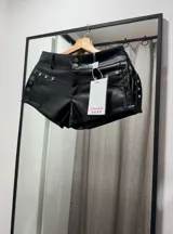Mini short negro de cuero sintético con tachas plateadas en forma de oso en los bolsillos delanteros y ojales metálicos en los laterales.