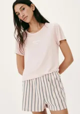 Pijama de dos piezas compuesto por una remera de manga corta color crema con un pequeño bordado de concha marina y un short de tiro alto con elástico y estampado de cuadrícula en tonos beige y blanco.