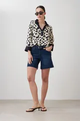 Blusa con estampa de margaritas blancas y verdes sobre fondo azul marino, con cuello polo y mangas 3/4 con puños en contraste.