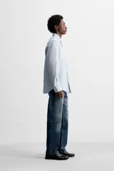 Camisa celeste a rayas verticales, de corte regular fit, confeccionada en tejido de algodón. Tiene cuello abotonado, manga larga con puños abotonados, bolsillo de parche en el pecho y cierre frontal con botones.