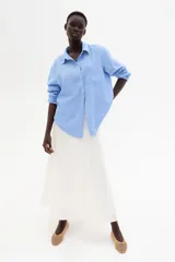 Camisa celeste de tejido liviano en mezcla de lino y viscosa, con cuello clásico, botones al frente, canesú de doble capa con pliegue de caja en la espalda, mangas largas con puños abotonados, bolsillo superior abierto y bajo redondeado.