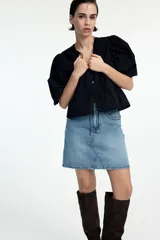 Blusa negra de algodón con textura de lunares, escote redondo con lazo, mangas tres cuartos abullonadas, botones frontales y cintura ajustable con cordón.