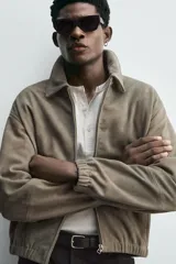 Cazadora de hombre color verde oliva, confeccionada en piel con acabado ante. Presenta un corte boxy fit, cuello solapa, cierre frontal de cremallera, bolsillos delanteros y elásticos en puños y bajo.