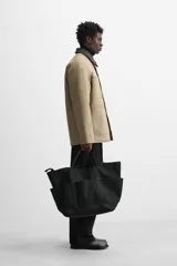 Parka negra de algodón con cuello solapa de cuero sintético, corte recto, acolchada, con bolsillos de parche y cierre frontal con botones.