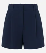 Short blanco de corte sastre, tiro alto, con pliegues frontales y trabillas en la cintura. Presenta solapas simulando bolsillos traseros.