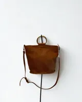 Cartera de cuero color marrón con correa larga ajustable y manijas circulares rígidas.