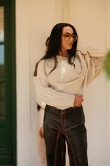 Buzo de tejido de punto color crudo, con cuello amplio que puede usarse caído sobre los hombros, mangas largas con trenzas de ochos y cuerpo con punto arroz.