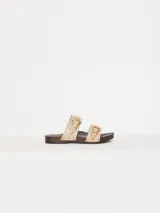 Zueco con capellada de cuero vacuno color crema, doble tira con hebillas metálicas doradas, base de madera con tachas y forrería interna de cuero.