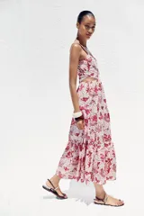 Vestido midi con estampado floral en tonos rosados, de escote recto y tirantes anchos con abalorios. Presenta aberturas laterales en la cintura y cierre trasero con cremallera oculta.