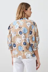 Camisa de manga 3/4 abullonada con puño elastizado, cuello mao y estampado floral en tonos azules y blancos sobre fondo tostado.