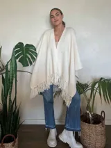 Ruana color crudo tejida a mano en punto arroz con lana merino. Presenta flecos en el borde inferior.