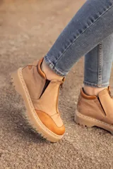 Bota de cuero color beige con puntera marrón, cierre frontal con cremallera y suela track.