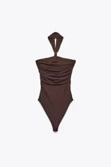 Body marrón de poliamida con cuello halter y pieza metálica dorada. Detalle de frunces y cierre inferior con botones a presión.