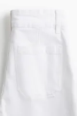 Pantalón de jean blanco, tiro alto, con pierna amplia y corte holgado. Presenta pliegues frontales y cierre de dos botones dorados.