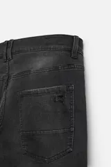 Pantalón de jean negro con corte skinny fit, cinco bolsillos, lavado con efecto roto y cierre frontal con cremallera y botón.