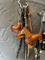 Llavero con dije de perro salchicha de ecocuero color marrón, dije de corazón y cordones decorativos.