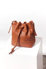Cartera tipo botellero color marrón, de cuero con efecto trenzado. Tiene correa regulable con hebilla para usar al hombro o cruzada, cierre con frunce y doble bolsillo interior, uno con cierre.