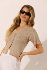 Remera corta de tejido de punto acanalado color beige, con cuello en V, mangas cortas y cierre frontal con botones. Presenta ribete naranja en el ruedo y las mangas.