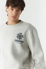 Buzo de felpa color gris claro con cuello redondo y puños y cintura acanalados. Estampado en la espalda con motivos de la naturaleza en tonos azul, verde y negro.
