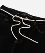 Pantalón masculino negro de corte baggy, confeccionado en sarga de algodón. Presenta detalles de costura, cierre tradicional de botón y cremallera, y un cordón blanco para ajustar la cintura.