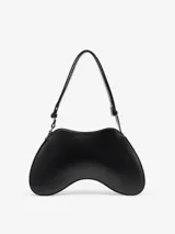 Bolso de mano negro de cuero con forma de joystick. Tiene correa de hombro desmontable y logo ovalado metálico en el frente.