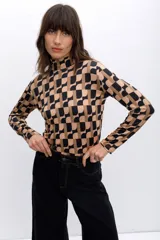 Polera de poliéster color beige con estampado geométrico en negro. Tiene cuello alto y mangas largas.