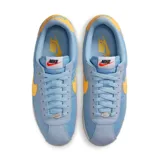 Championes Nike Cortez celestes con detalles en amarillo y suela blanca.