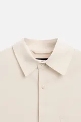 Camisa color crema de corte regular fit, confeccionada en tejido con viscosa. Tiene cuello solapa, manga larga con puños abotonados, bolsillo de parche en el pecho y cierre frontal con botones.