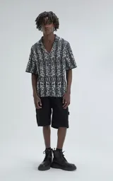 Camisa de manga corta tejida de punto abierto (símil crochet), calce oversize, color negro con diseño abstracto en beige.