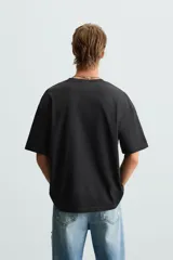 Camiseta negra de corte relaxed fit, cuello redondo y manga corta. Estampado frontal con la frase "Impact Nexus" y otros logos pequeños.