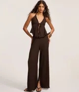 Blusa marrón oscuro con textura plisada, estilo frente única (halter) con escote en V profundo y lazo ajustable en el centro del busto. Presenta un ruedo con volado o efecto nube.