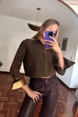 Camisa corta marrón de cuero ovino desgastado con cuello clásico, cierre frontal con botones y mangas largas con aberturas.