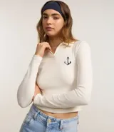 Blusa de manga larga color crema, con cuello polo, escote en V y bordado de ancla en el pecho.