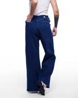 Pantalón de denim azul con corte sastrero de pierna ancha, tiro alto, cierre frontal invisible y pretina cruzada. Aplique de caballo/dragón en bronce hecho a mano y bordado negro del logo Temblad en la parte trasera.